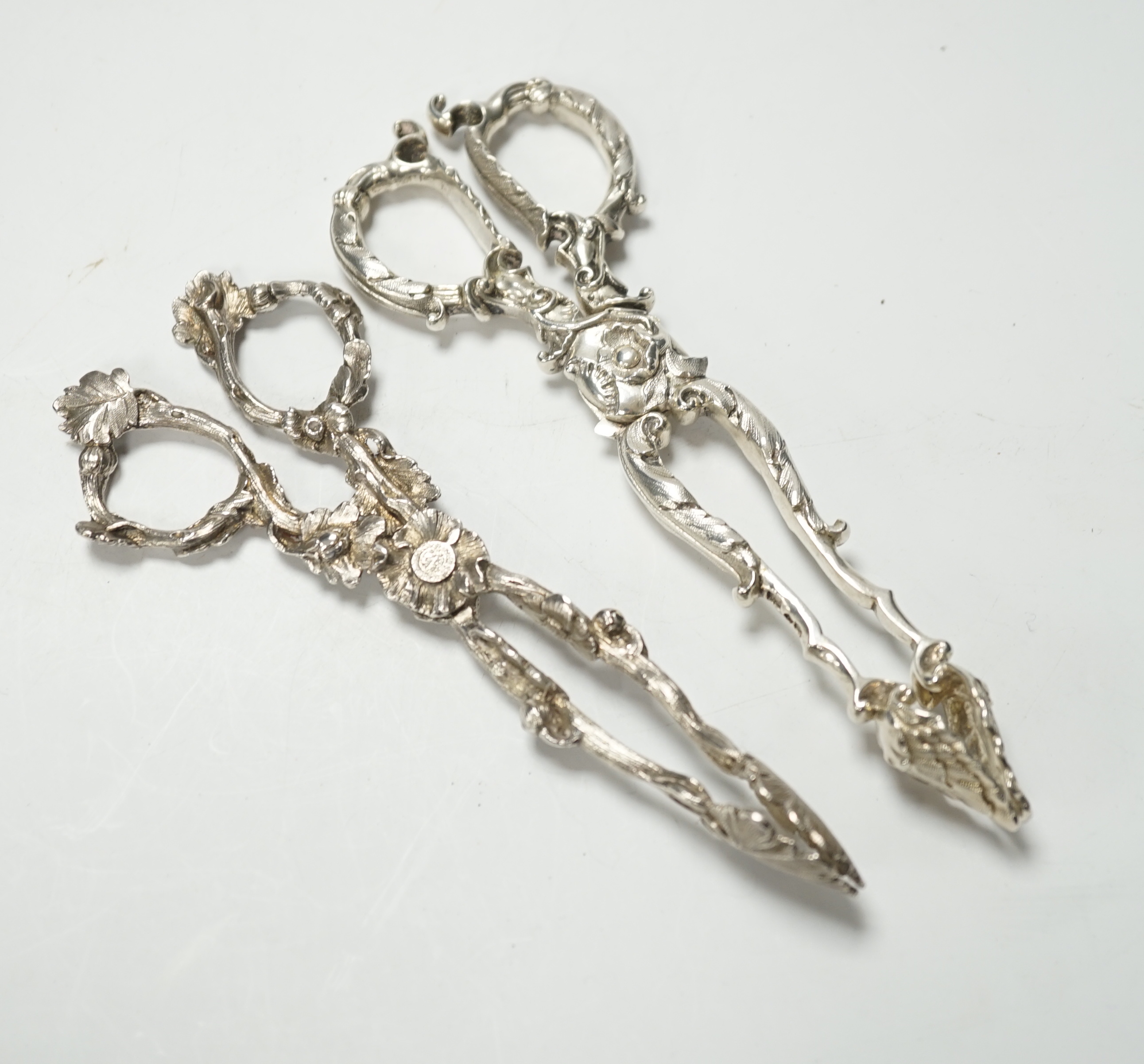 A pair of Victorian cast silver sugar tongs, of foliate design, by George Adams, London, 1871, 14.2cm and a pair of William IV cast silver sugar tongs, by Theobalds & Bunn, London, 1835, 15.4cm, 102 grams.